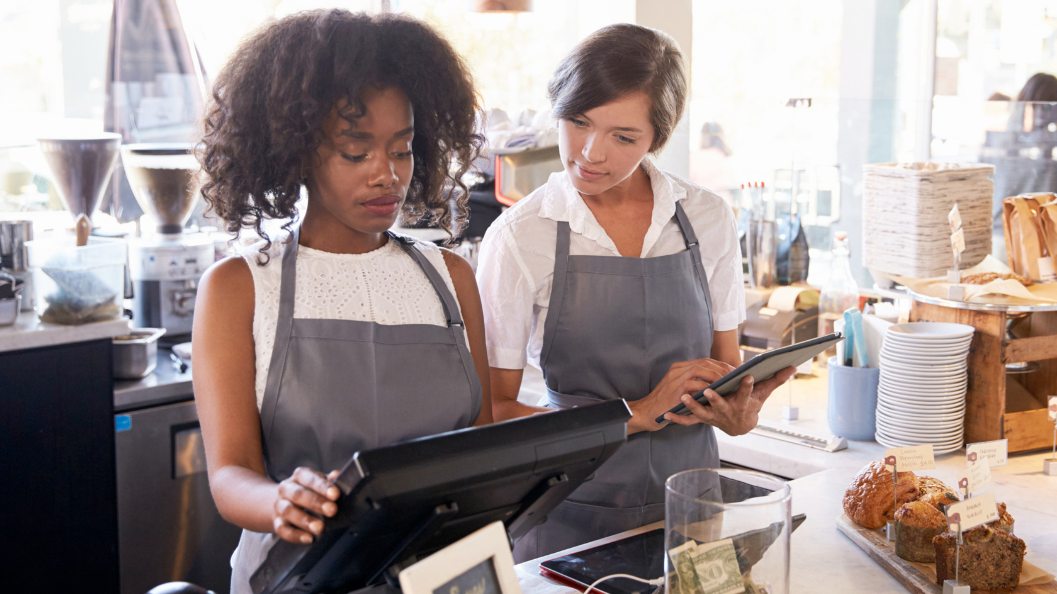 Deux femmes employées derrière un comptoir regardent une caisse enregistreuse sur un point de vente de restauration