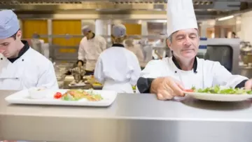 Dans la cuisine d'un restaurant, un chef transmet un plat à l'équipe du service